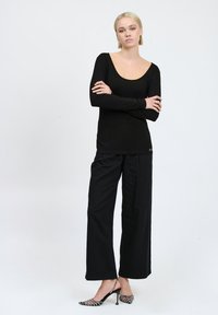 Maglietta nera a maniche lunghe con scollo rotondo, abbinata a pantaloni neri a gamba larga e tacchi neri decorati con punta affusolata.