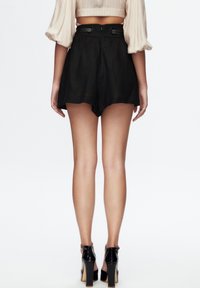 Sorte shorts med høj talje og vide ben, med to knapper bagpå og et glat stof. Bruges med sorte højhælede sko.
