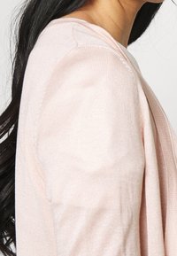 Světle růžový kardigan z měkké texturované směsi bavlny. Má jednoduchý design, viditelné švy a uvolněný střih s lehkým převisem na jedné straně.