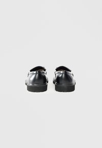 Czarne skórzane buty z okrągłym czubkiem, płaską gumową podeszwą i szczegółami w postaci tylnego pasku. Gładka tekstura, minimalistyczny design i brak widocznych wzorów.