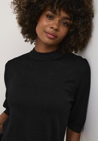 Top negro de punto con un escote alto y mangas cortas, que presenta un brillo sutil y una textura suave. Diseño simple y ajustado.