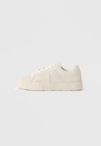 Sneaker bianche in suede con suola in gomma texturizzata, pannelli cuciti e un sottile logo dorato. Design low-top con lacci tondi.