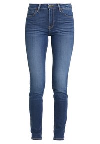 Jeans ajustados en denim azul oscuro con un ligero desgaste. Presentan un diseño clásico de cinco bolsillos y herrajes de metal en la cintura.