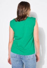 Groen, kort mouwtop met een ronde halslijn en een ontspannen pasvorm, gecombineerd met lichtblauwe denim jeans met achterzakken.