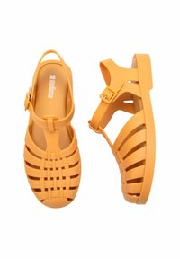 Infradito gialle in plastica flessibile con design intrecciato. Fascetta regolabile con fibbia e suola piatta. Stile aperto davanti, texture leggera.