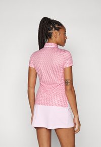 Kortærmet polo shirt i pink med et geometrisk mønster, der har en krave, samt en lyserød nederdel lavet af let, strækbart stof.