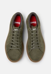 Sneaker in suede verde con suole in gomma marrone. Presentano un design con lacci e solette rosse con il marchio "CAMPER" in bianco.