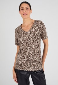 Beige V-hals T-shirt met een luipaardprint in zwart en bruin, korte mouwen, gemaakt van zachte stof, gecombineerd met zwarte broeken.