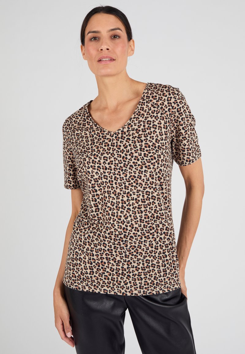 Beige V-hals T-shirt met een luipaardprint in zwart en bruin, korte mouwen, gemaakt van zachte stof, gecombineerd met zwarte broeken.