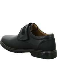 Scarpa in pelle nera con punta arrotondata, chiusura con cinturino in velcro e suola testurizzata. Il design include dettagli in cucitura e un interno imbottito.