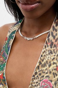Colar de prata com um pendente em forma de script que diz "F**k Marry", adornado com pérolas brancas. Disposto sobre um tecido colorido e estampado.