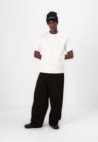 Weißes Baumwoll-T-Shirt, lockere Passform, kombiniert mit schwarzen weit geschnittenen Hosen. Schwarze Mütze mit weißem Text. Glatte Texturen, minimalistisches Design.