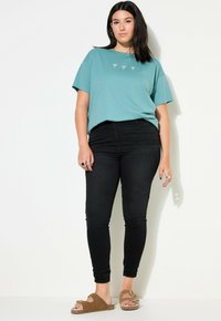 Camiseta de algodón color teal con mangas cortas y un corte relajado. Combinada con jeans skinny negros y sandalias marrones con detalle de hebilla.