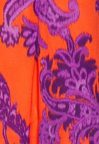 Tessuto arancione con un motivo paisley viola, caratterizzato da spirali e dettagli intricati. La texture appare liscia e vibrante.
