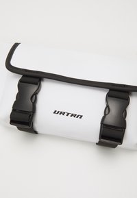 White waterproof bag with black hardware, featuring two adjustable buckle closures and URTRN logo. Smooth texture, flat rectangular design.