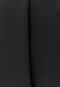 Schwarzer Stoff, der aus der Nähe das weiche, strukturierte Material mit geschwungenen Nähten und einer glatten Oberfläche zeigt. Keine sichtbaren Muster oder Akzente.