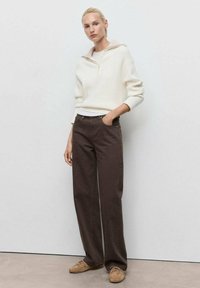 Cream, ribbed sweater with a zip collar, paired with brown wide-leg pants. Footwear is tan with laces. Minimalist design, neutral colors.