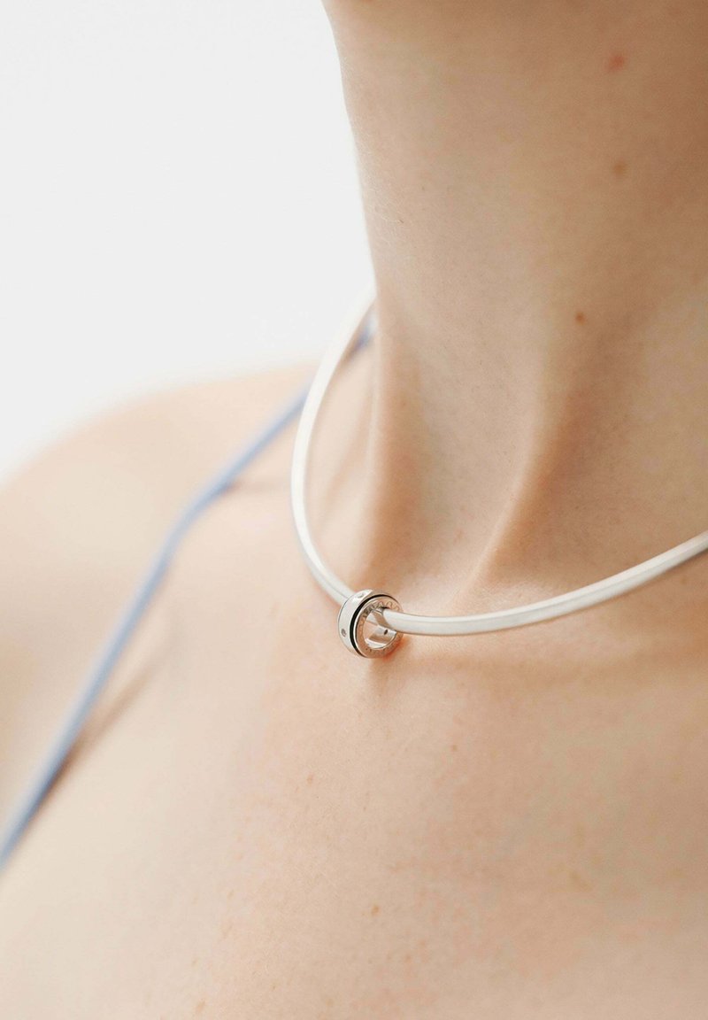 Collar choker blanco con un acento circular de plata. Textura suave con un diseño elegante, que presenta un detalle central de anillo de plata.