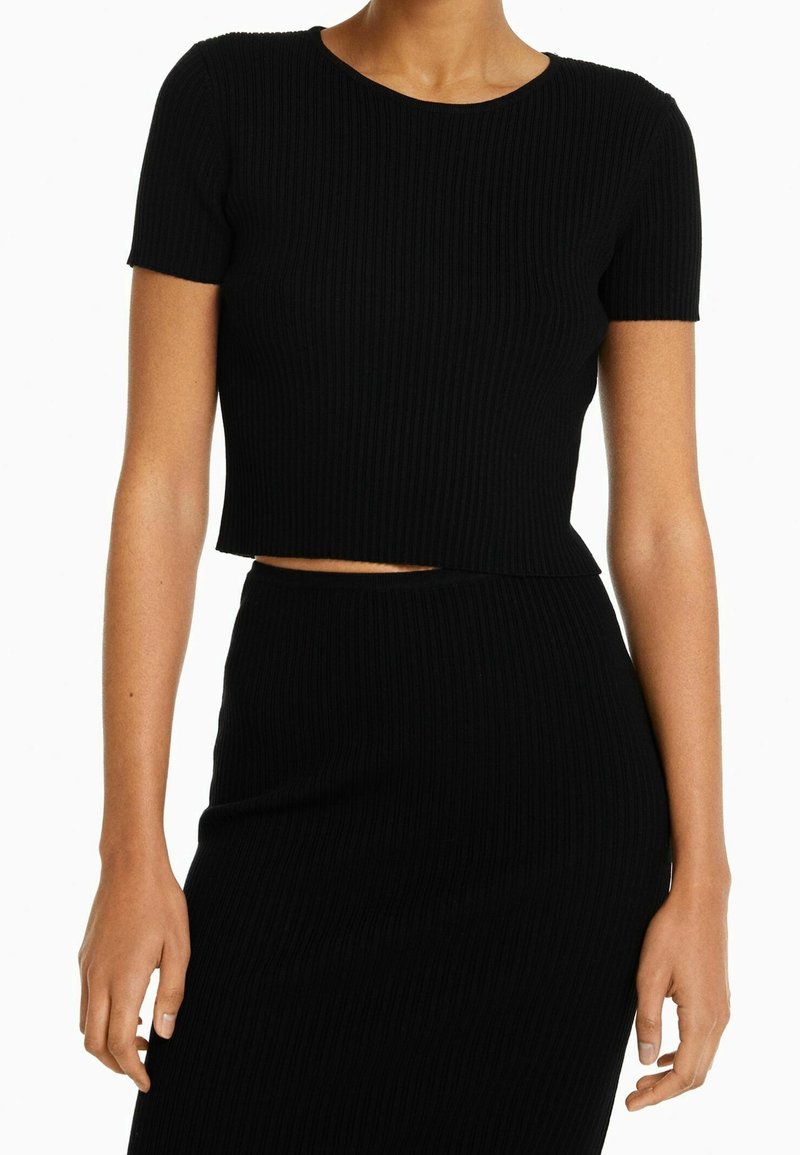 Svart ribbad crop top med korta ärmar och rundad halsringning. Tyget har ett strukturerat mönster och är skuret ovanför midjan.