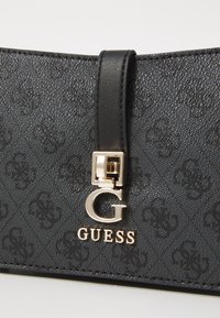 Schwarze strukturierte synthetische Handtasche mit einem goldfarbenen Verschluss und einem auffälligen 'G'-Logo. Verfügt über einen glatten Ledertrageriemen und ein geprägtes Muster.