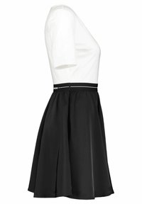 Svart och vit klänning med en åtsittande vit överdel med korta ärmar och en flödande svart kjol, accentuerad med ett svart midjeband med vita ränder.
