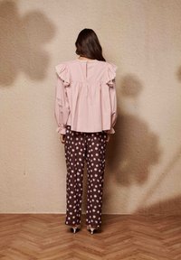 Ροζ μπλούζα με βολάν στα μανίκια και άνοιγμα στην πλάτη, συνδυασμένη με παντελόνι καφέ με πουά πουά; λείο ύφασμα και χαλαρές, ρέουσες γραμμές.