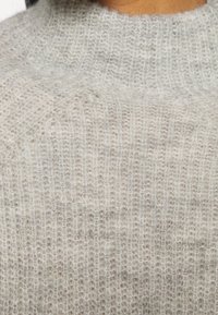 Pull gris clair, duveteux, en maille côtelée avec une vue en gros plan de la poitrine et de la zone du cou.