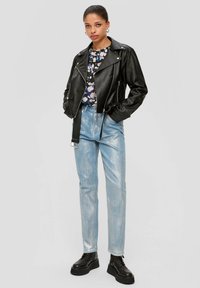 Zwarte leren motorjack over een blouse met bloemenpatroon, gecombineerd met lichtblauwe high-waisted jeans en zwarte platformlaarzen.