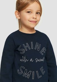 Marineblauwe sweatshirt met de tekst "SHINE with a sweet SMILE" in zilveren rhinestones. Crew neck ontwerp met een zachte textuur.
