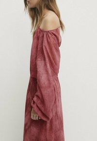 Robe décolletée en rose pâle, fabriquée dans un tissu léger avec des manches amples et une taille cintrée pour un look décontracté.