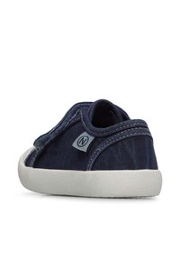 Navy canvas shoe with a low profile design, textured white rubber sole, and a side logo tag. Stitched accents enhance the minimal style.
