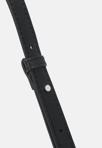 Svart läderrem med vit sömnad, flera justeringshål och en silverfärgad metallnubb. Slät yta och en flexibel design.