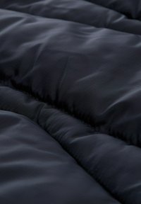 Granatowy pikowany materiał o gładkiej fakturze i widocznych liniach st stitching. Zawiera subtelny wzór siatki, podkreślający ciepło i izolację.