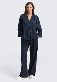Navy patterned blouse with a v-neckline and long sleeves, paired with loose-fitting navy trousers and white sneakers.