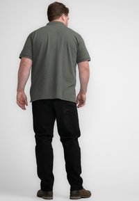 Groene polo met korte mouwen van een gestructureerde stof, gecombineerd met zwarte broek en bruine schoenen. De achteraanzicht toont een klassiek kraagontwerp.