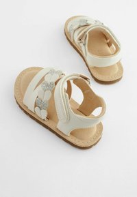 Weiße Sandalen mit glitzernden silbernen Herzakzenten. Hergestellt aus synthetischem Material mit einer weichen beigen Innensohle und einer braunen Gummisohle. Offenes Design.