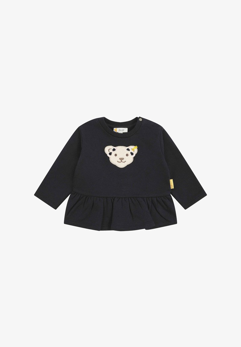 Top de manga larga azul marino con un aplique texturizado de cara de oso y un dobladillo con volantes. Presenta botones en los hombros y una etiqueta en el costado.