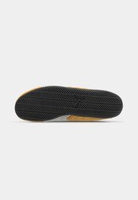 Sneakersohle mit einem schwarzen Gummiprofil, grauen Seitenakzenten und einem gelben Detailbereich, der strapazierfähiges Material und Traktion betont.
