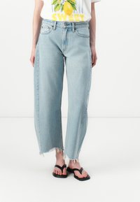 Lichtblauwe wijd-uitlopende jeans met gefranjerde randen, gemaakt van denim, met een middelhoge taille. Gepaard met zwarte slippers en een graphic t-shirt.