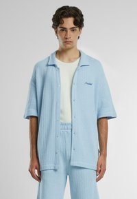 Light blue knit button-up shirt with short sleeves and a collar, paired with matching shorts. Features an embroidered "Prohibited" detail.