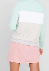 Sudadera con paneles horizontales en azul claro, blanco y gris; combinada con una falda de mezclilla rosa. Presenta puños y dobladillo acanalados.