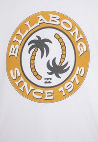T-shirt bianco in cotone con una grafica circolare che presenta palme nere, accenti arancioni e la scritta "BILLABONG SINCE 1973" in lettere grasse.
