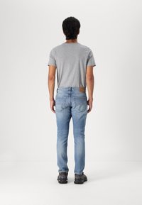 Camiseta gris claro, vaqueros azul denim y zapatillas negras. Los vaqueros tienen bolsillos traseros y una etiqueta de cuero marrón en la cintura. Diseño ajustado.