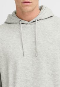 Sudadera de algodón gris claro con capucha ajustable, que presenta una textura suave y un corte holgado. No hay patrones ni acentos visibles.