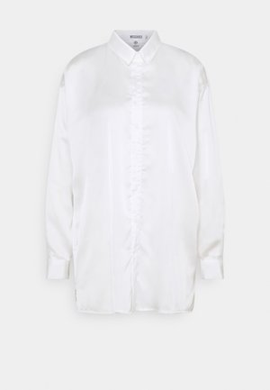 Biała satynowa koszula z długim rękawem, zapinana na guziki z przodu i z ostrym kołnierzykiem, prezentowana na jasnoszarym tle.