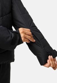 Czarna kurtka puchowa o teksturowanym wykończeniu, z kieszenią na zamek na ramieniu i mankietem na rzep, podkreślona eleganckim, zbudowanym designem.