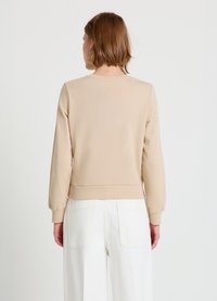 Sweat-shirt beige en mélange de coton avec poignets et ourlet côtelés, doté d'un col rond classique et d'une texture lisse. Associé à un pantalon blanc à jambes larges.