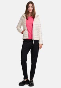 Gevoerde roomkleurige jas met een capuchon, roze trui eronder, zwarte tapered broek en zwarte platform schoenen. Ritszakken op de jas en broek.