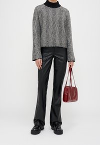 Svetr s herringbone vzorem v černobílé, černé kožené kalhoty s rozšířenými nohavicemi, červená kabelka a masivní černé boty se hřebíkovými akcenty.