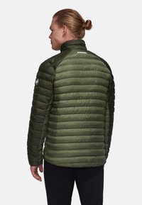 Grön puffjacka med kviltad textur, hög krage och logotypdetalj på axeln. Lättviktig och åtsittande design, lämplig för utomhusbruk.